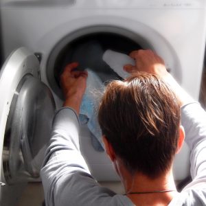 A Woman Putting Clothing Into A Washing Machine